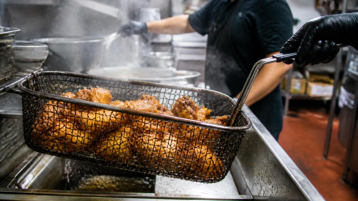 Cook lifting a fryer basket of golden chicken wings to ensure safe gluten free wing options in Peachtree Corners.
