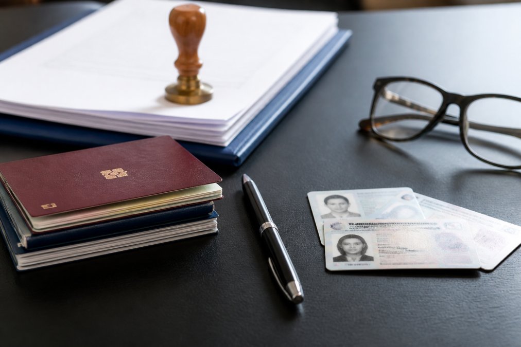 Close-up of passport, identification documents, and notary paperwork arranged on a desk with a pen and glasses, natural office lighting