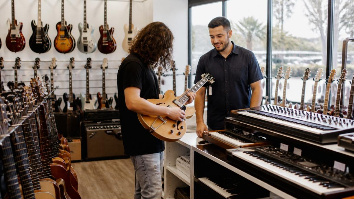 Staff member assisting a customer inside a bright gold coast musical instrument shop filled with guitars