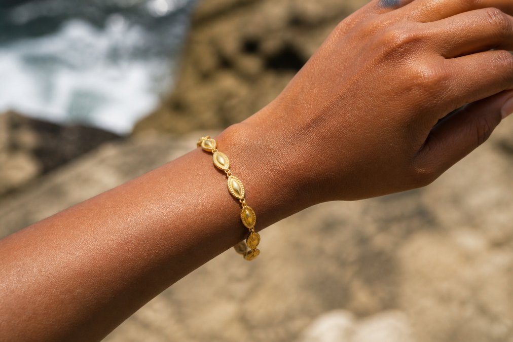 Woman's hand wearing a delicate gold-plated brass bracelet, showing the jewelry detail and warm golden finish against her skin during daylight, with the bracelet sitting naturally on her wrist