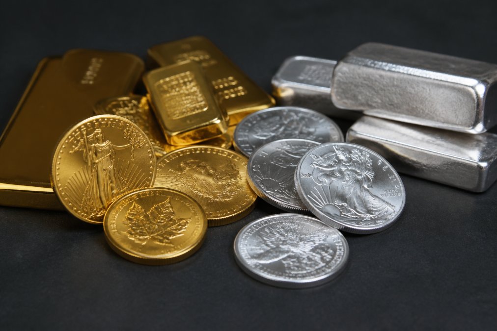 Close-up of gold and silver bullion coins and bars arranged on a dark surface, showing distinct color and finish differences between the two metals