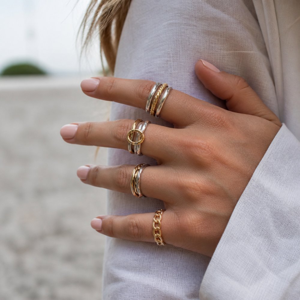 Close-up of a woman's hand displaying multiple stacked rings combining warm yellow gold and cool silver bands on different fingers, showing elegant mixed-metal styling with natural daylight highlighting the contrast