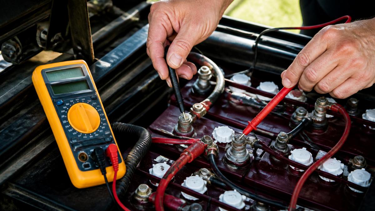 Hands using a multimeter to test golf cart battery voltage to diagnose golf cart hesitation inclines.