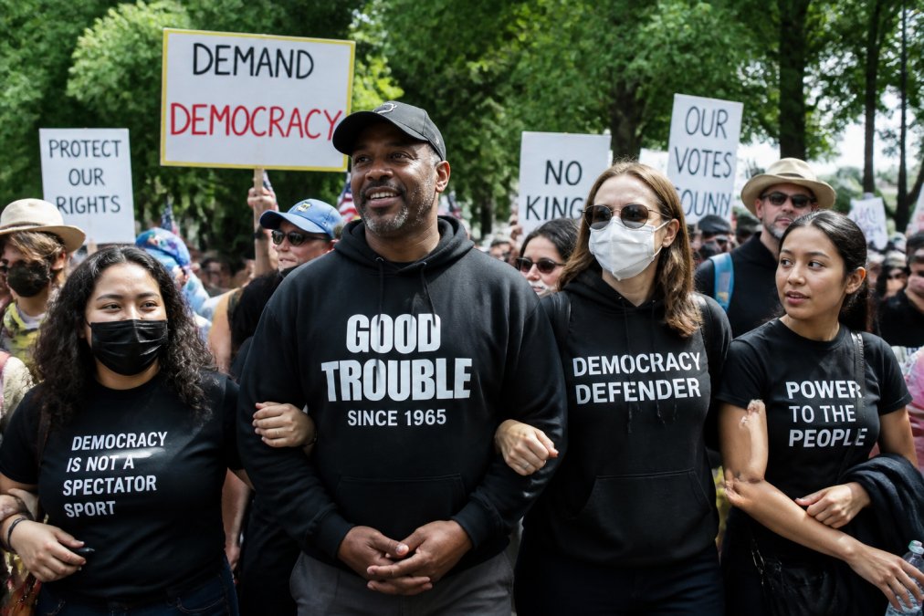 Diverse group of activists wearing statement hoodies and tees at an outdoor march, displaying visible protest messages and unity, natural daylight with banners in background