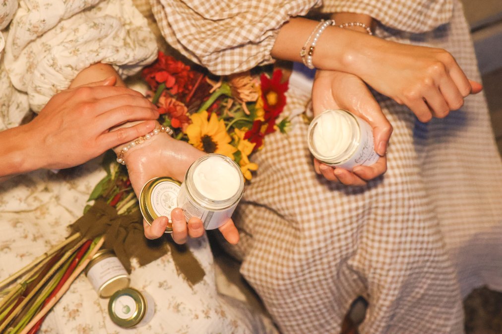Close-up of two people applying tallow and holding jars of tallow body balms.