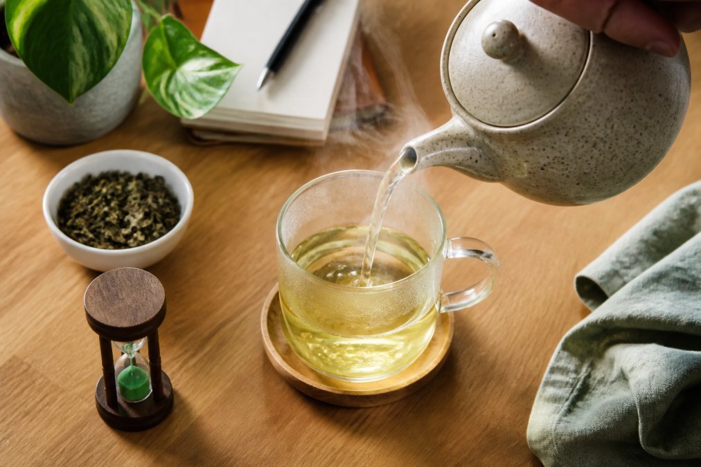 Steaming green tea for focus being poured into a clear glass cup on a wooden desk with a timer nearby