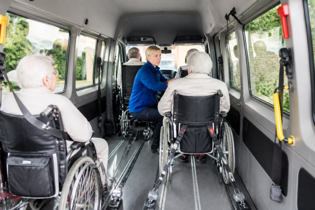 Een zorgmedewerker die samen met meerdere rolstoelgebruikers in een professioneel groepsvoertuig zit, met duidelijk zicht op de veiligheidsvoorzieningen, rolstoelverankering en de professionele, schone omgeving van het voertuig