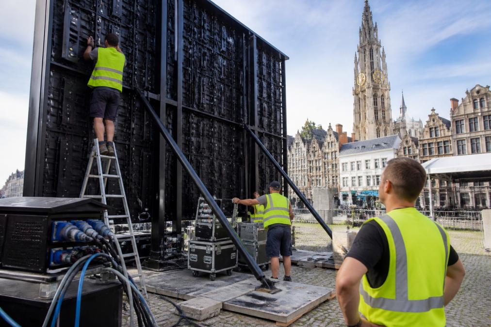 Professioneel team dat een groot LED-scherm installeert op een buitenevenement in Antwerpen, met elektriciteitsverbindingen zichtbaar, veiligheidsmaatregelen aangebracht, en technicus controlerende beeldkwaliteit in daglicht
