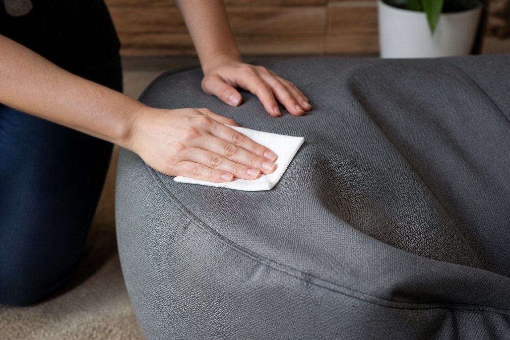 Gros plan des mains nettoyant une housse de beanbag avec un tissu humide, montrant la facilité d'entretien et la texture du tissu résistant