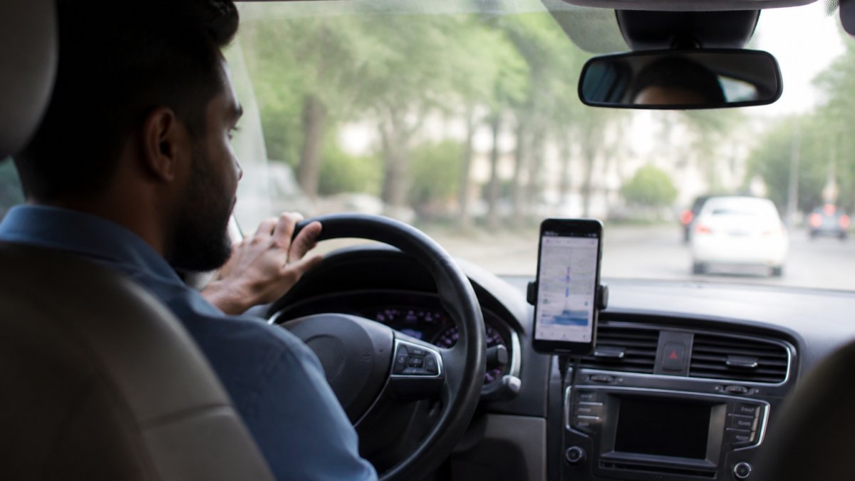 Rideshare driver sitting in vehicle with smartphone displaying active rideshare app on dashboard, showing the moment when coverage periods matter during a shift