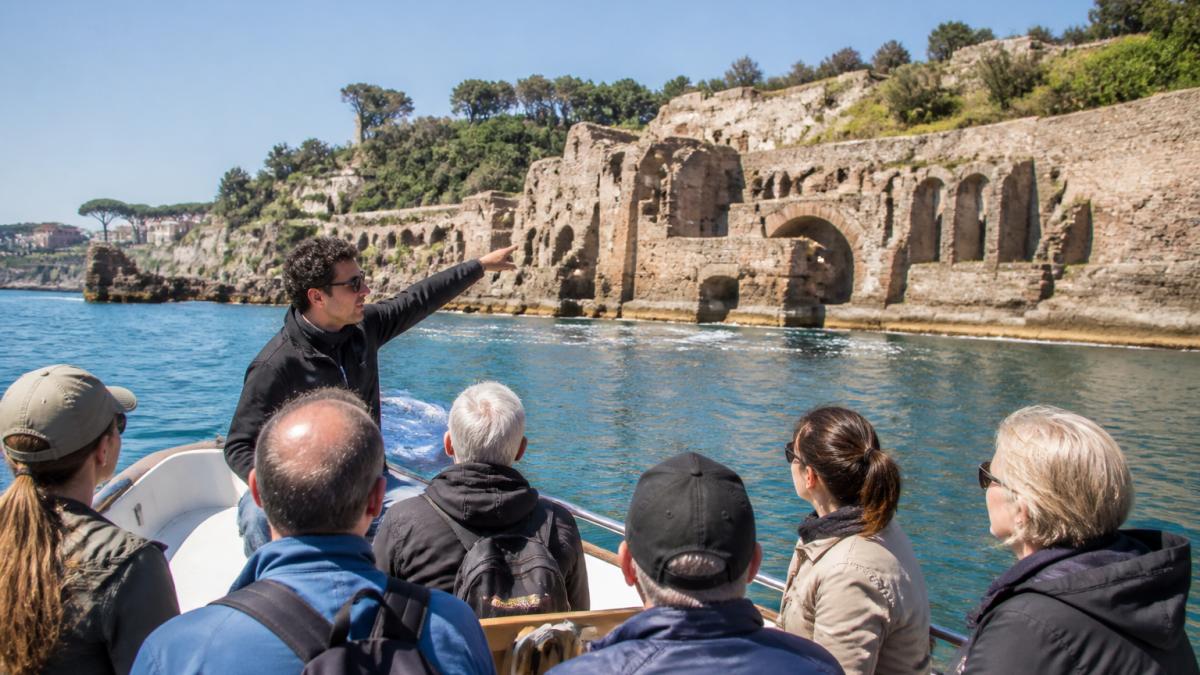 Tourists on a boat observing ancient ruins during guided tours of sunken ruins in the sunny Baia coastline