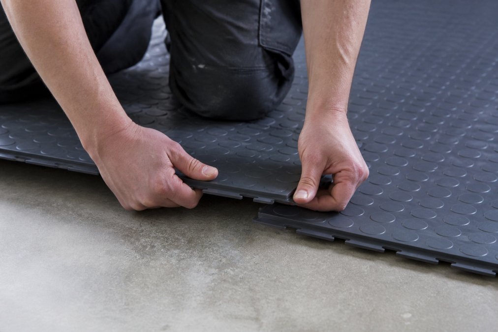 Close-up of hands pressing two Fortelock PVC tiles together using the click-system, showing the interlocking edges connect without glue on a concrete workshop floor