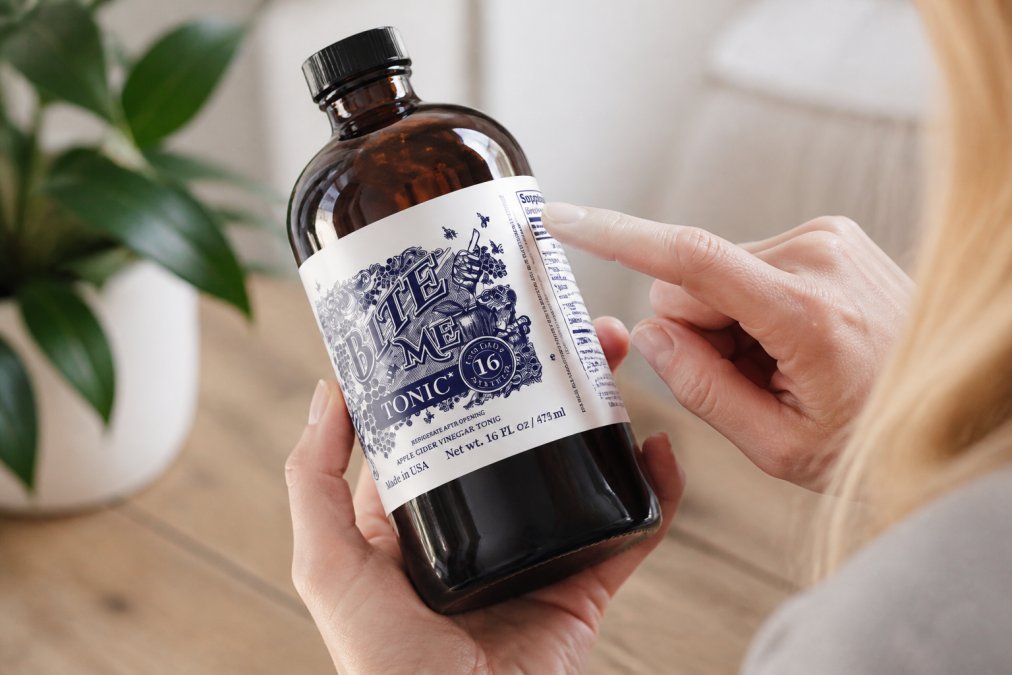 Close-up of hands holding a supplement bottle with the ingredients label clearly visible in bright natural light, showing someone reading the fine print carefully