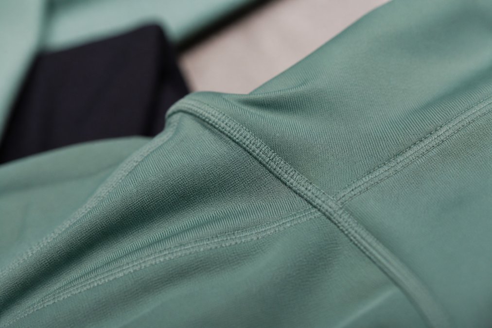 Close-up of seamless construction and reinforced stitching detail on high-quality activewear fabric, showing technical textile weave and precision seaming under natural light