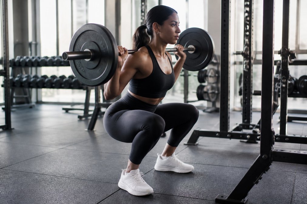 A female athlete performing a deep squat in a bright, modern gym, wearing high-waisted leggings, with a focus on the fabric's opacity and fit