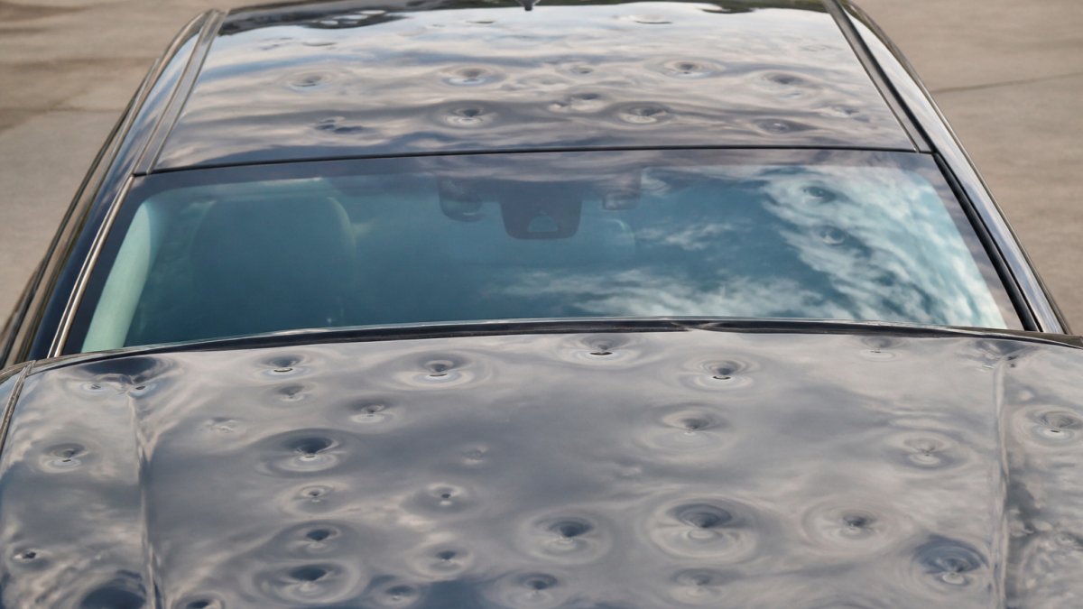 Close-up of a vehicle's hail-damaged hood and roof showing multiple small and medium dents with intact paint, illustrating typical hail damage patterns