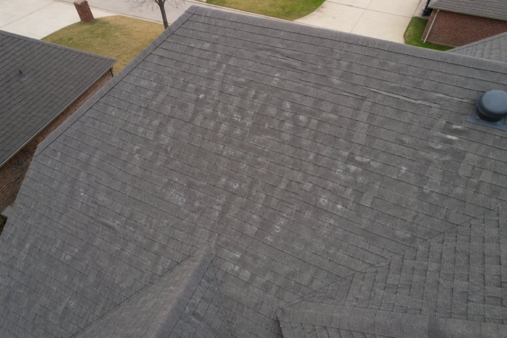 Aerial drone view of a residential neighborhood roof showing scattered hail impact marks across shingles with visible granule loss