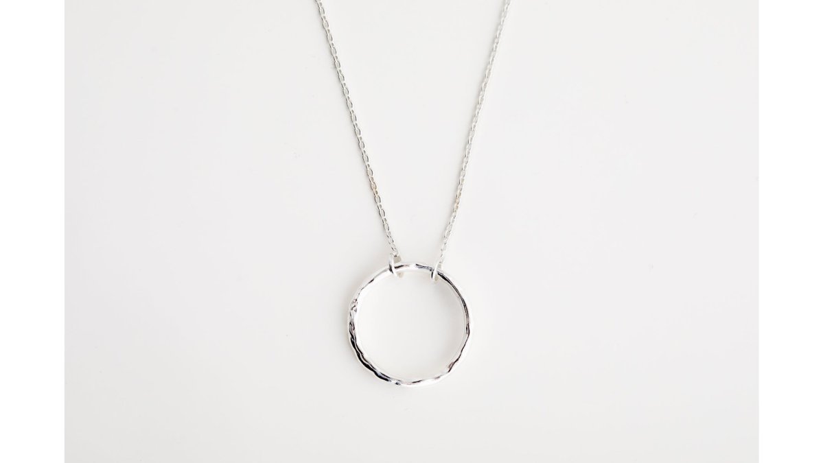 Flat lay arrangement of minimalist jewellery pieces on a neutral linen background: delicate hammered disc stud earrings, fine-link chain necklace in gold vermeil, and open circle stackable rings arranged to show how pieces complement each other in soft natural daylight