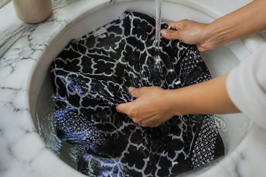 Hands gently rinsing a hand block printed cotton kaftan in cool water in a sink, showing careful washing technique with delicate water pressure