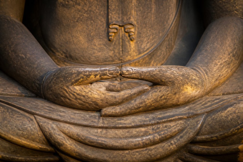 Close-up of a Buddha statue's hands showing intricate finger positioning and sacred hand placement in a specific mudra gesture, with soft golden lighting highlighting the carved craftsmanship and subtle details
