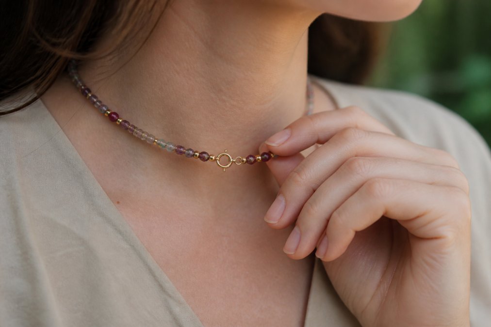 Close-up of a woman's hand wearing a delicate gemstone necklace, showing natural stone details and gold clasp in soft natural daylight