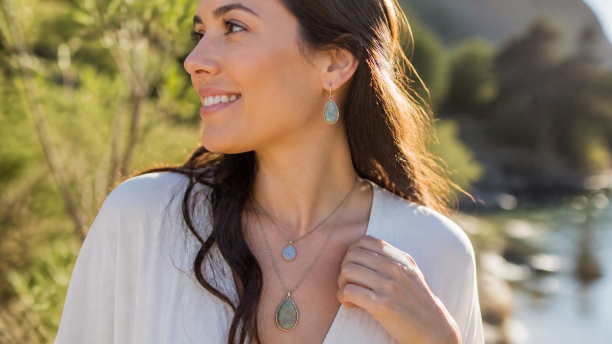 Woman smiling while wearing layered necklaces and gemstone earrings in warm sunlight