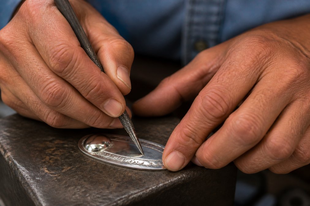 Close-up of a master Navajo silversmith's hands working on stamped silver detail with traditional tools, showing the precision and craftsmanship of handcrafted jewelry