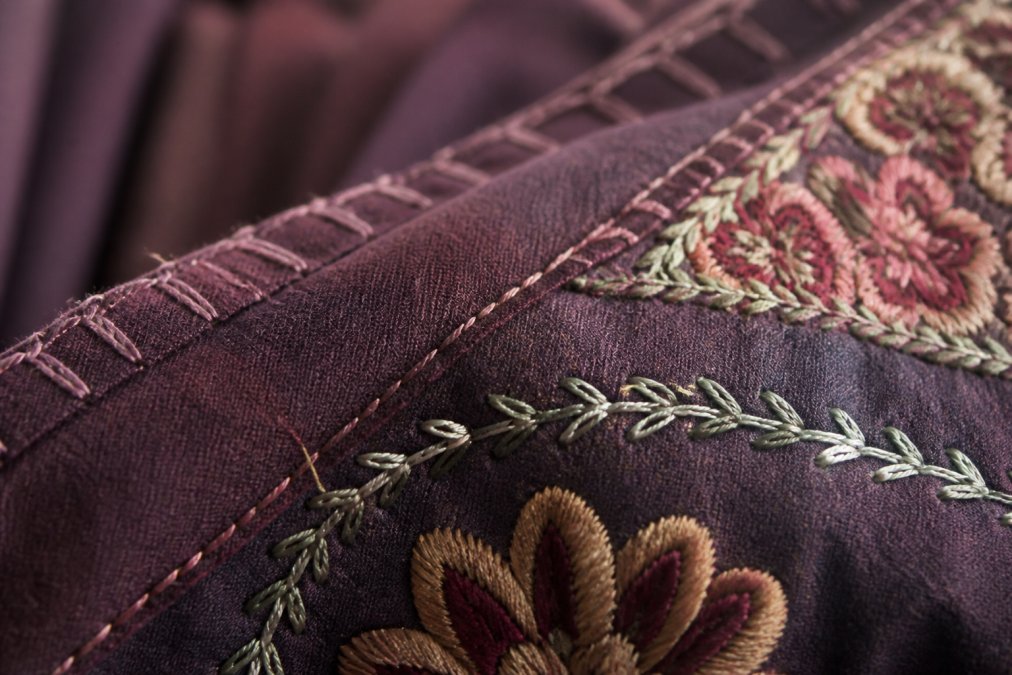 Close-up of intricate hand-stitched seams and fine embroidery detail on a bohemian garment showing precise needle work and quality thread construction
