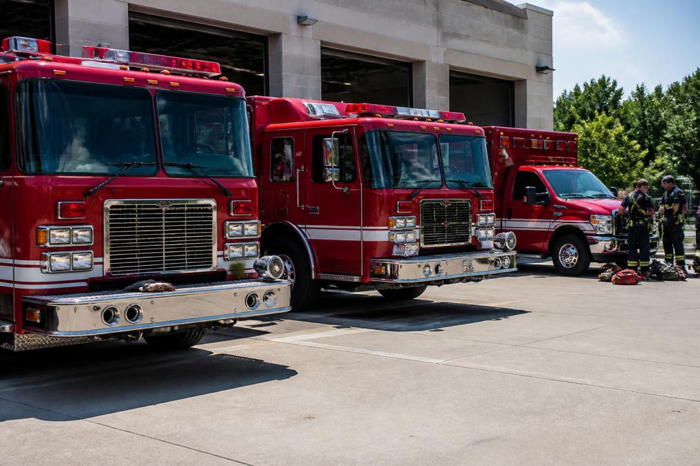 Multiple emergency response vehicles lined up at a station, showing coordination and organization needed for efficient emergency response, with responders visible in background preparing equipment