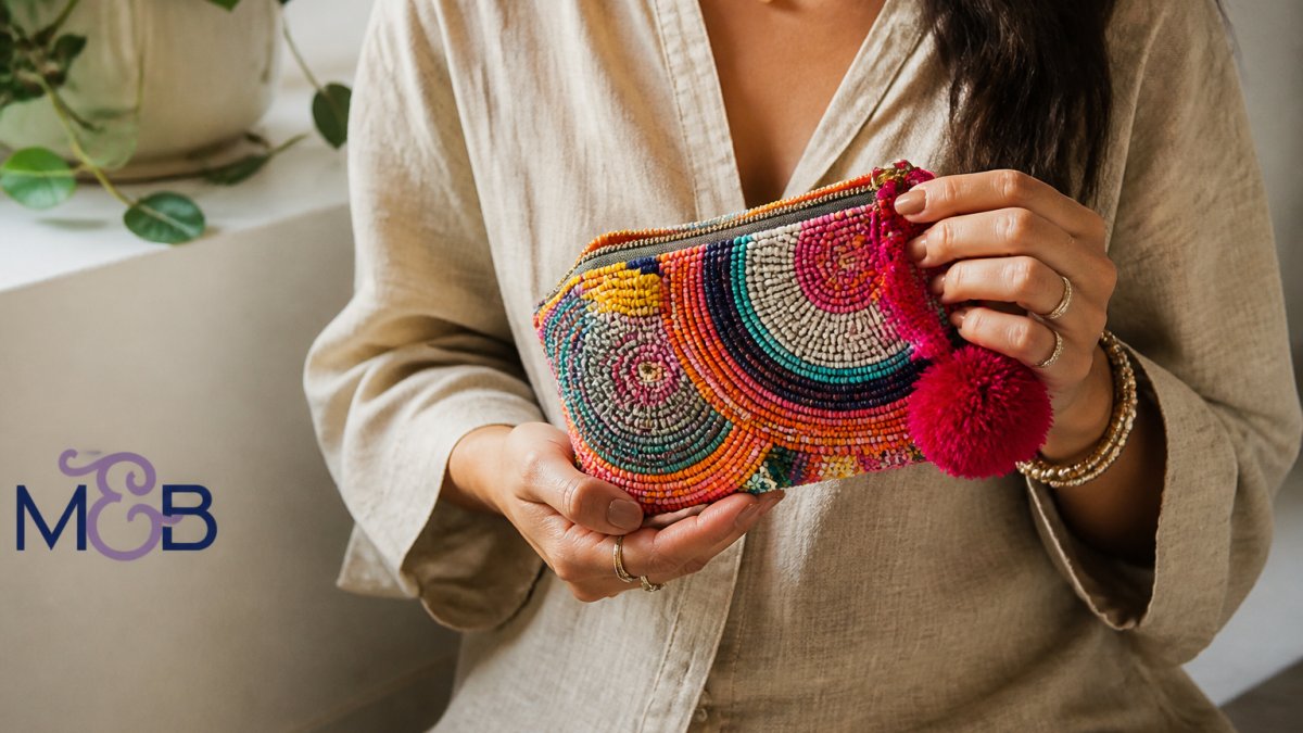 Close-up of a woman's hands holding a vibrant beaded coin purse with pom-pom zipper, styled on a neutral linen outfit, soft natural light