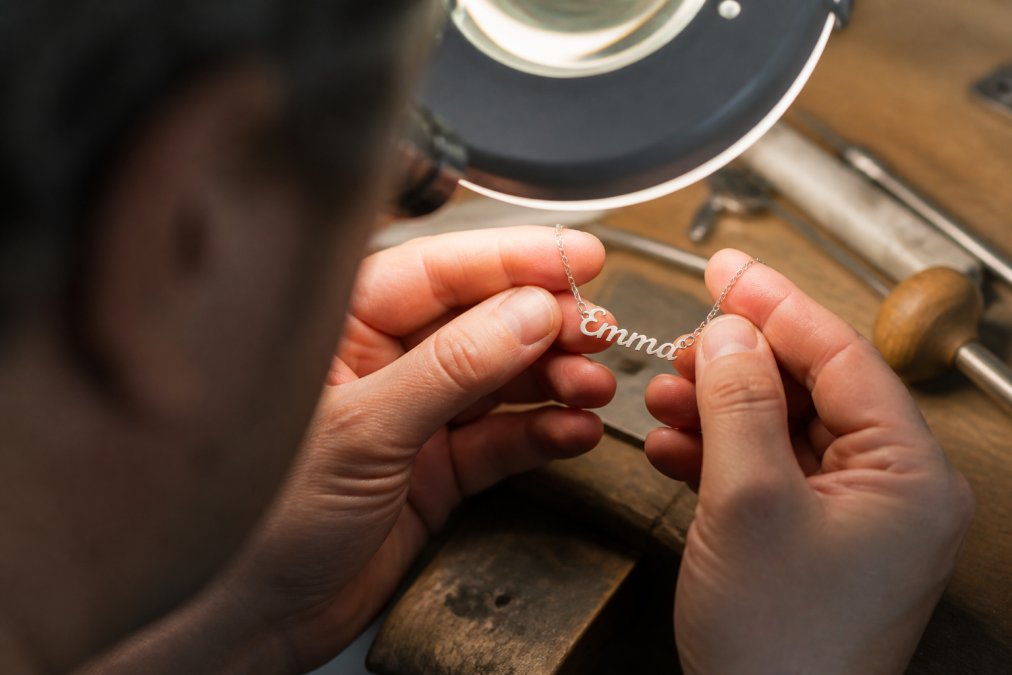 Close-up of hands carefully examining the fine detail work and metal finish of a personalized handcrafted necklace pendant under bright studio lighting