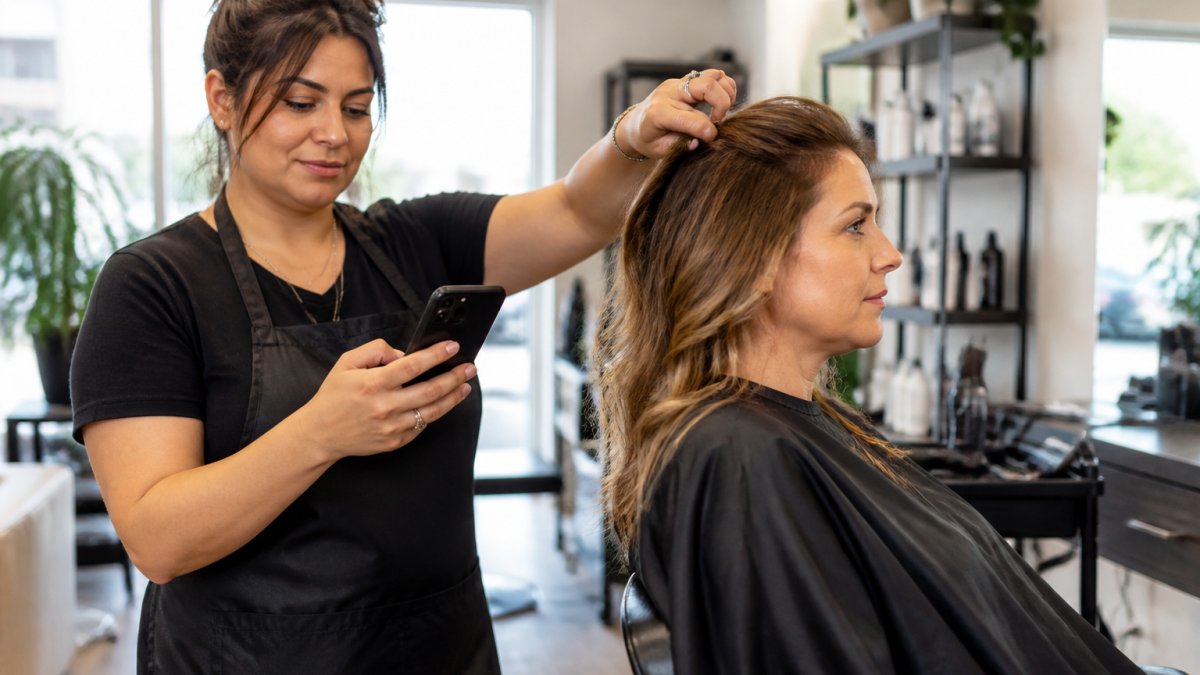 Busy salon owner checking her smartphone while attending to a customer, showing focus on client service rather than marketing tasks