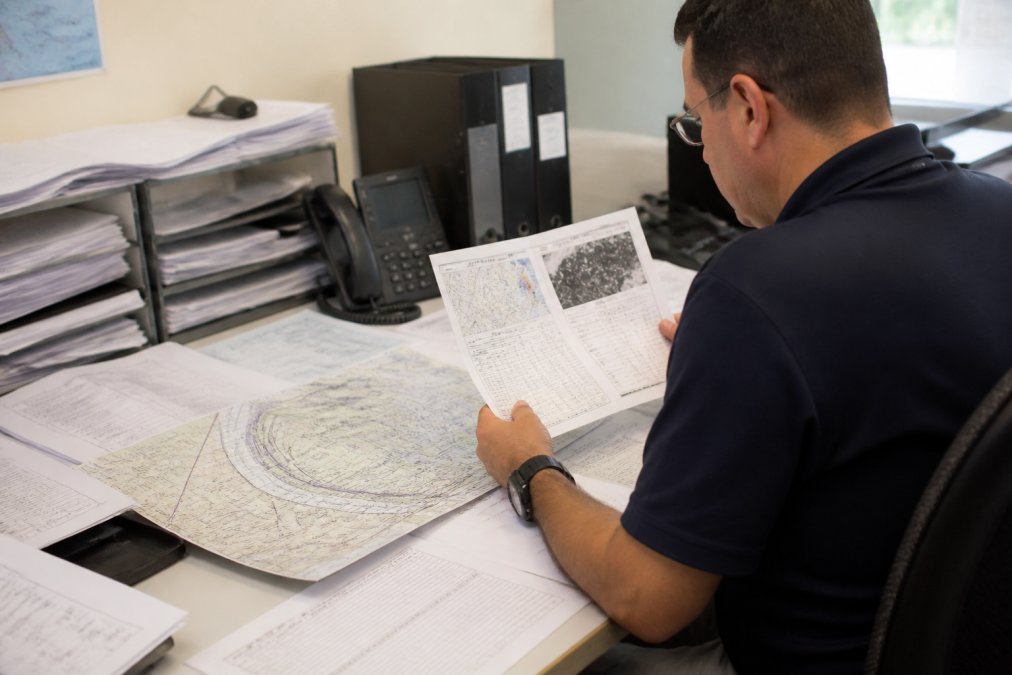Experienced airline dispatcher reviewing printed weather briefing materials and aeronautical charts at a desk with multiple weather reports and a computer monitor displaying METAR data
