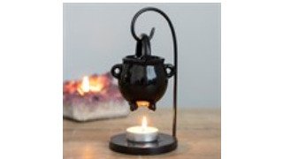 A styled flat lay of aromatherapy products on a rustic wooden table: a portable ultrasonic diffuser emitting a soft mist, small amber glass essential oil bottles, and a hanging cauldron oil burner with a lit tea light beneath it