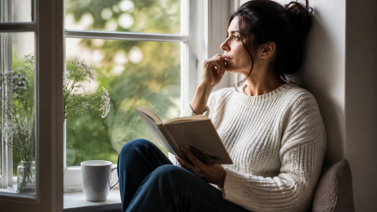Person sitting by a window reading healing poetry with a cup of tea in a calm, reflective atmosphere.