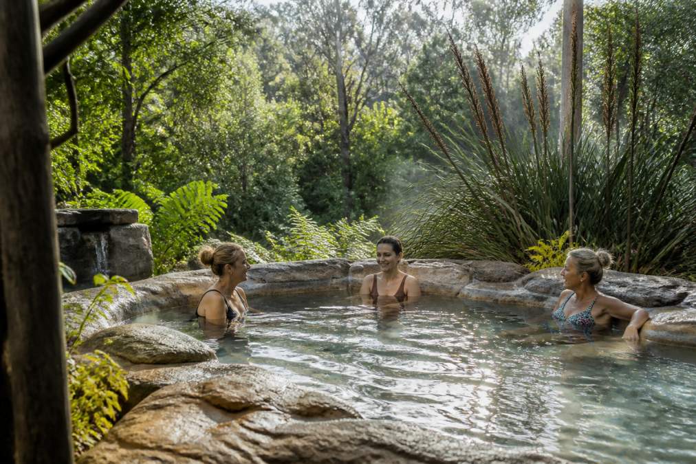 Small intimate group of guests in peaceful thermal spa setting surrounded by native vegetation and natural stone, conveying exclusivity and serene atmosphere