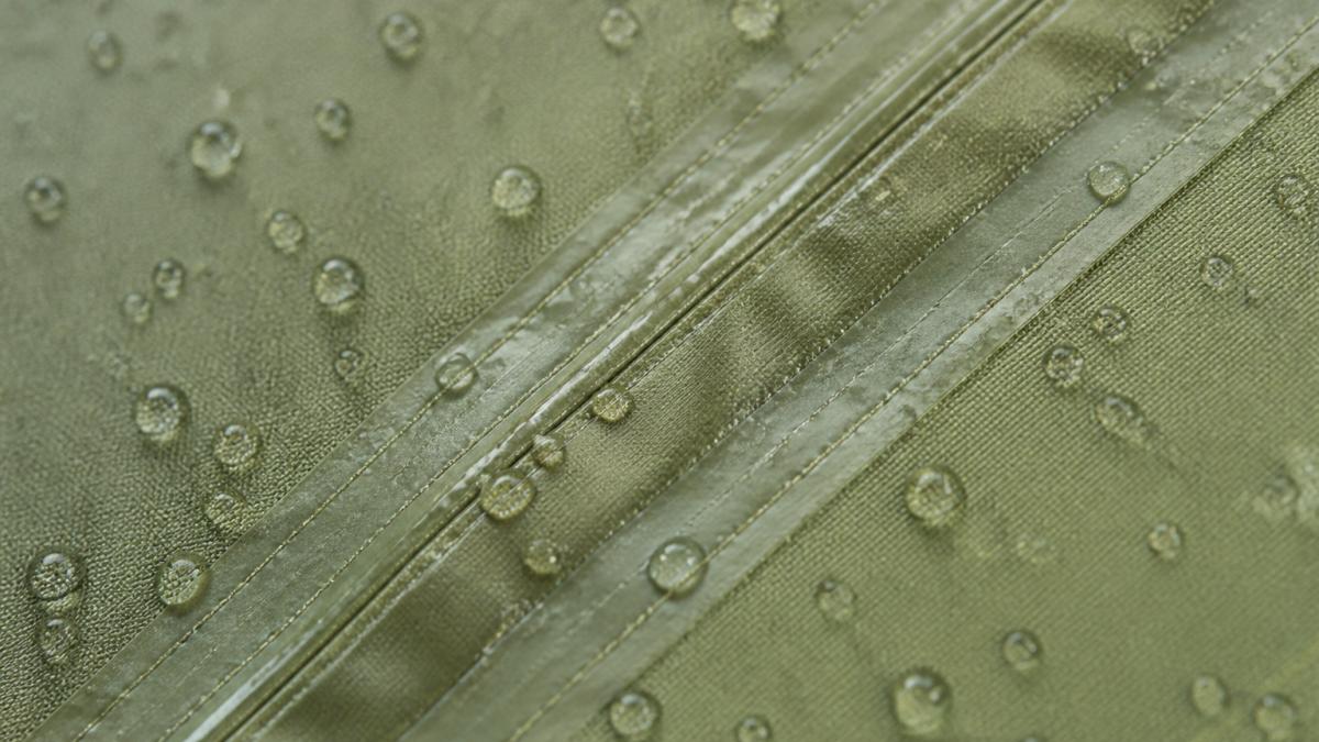 Close-up of tent fabric showing tight polyester weave with water droplets beading on sealed seam, natural outdoor lighting highlighting fabric texture and stitching detail
