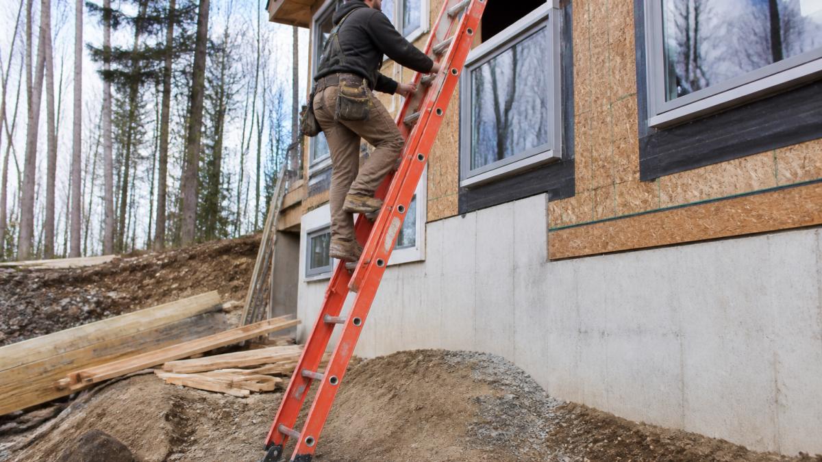 Construction worker safely climbing a heavy-duty fiberglass ladder on an uneven job site terrain