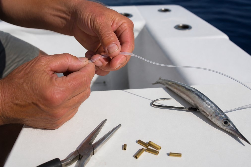 Angler sliding heavy duty leader tubing onto a monofilament line next to a rigged ballyhoo on a boat deck