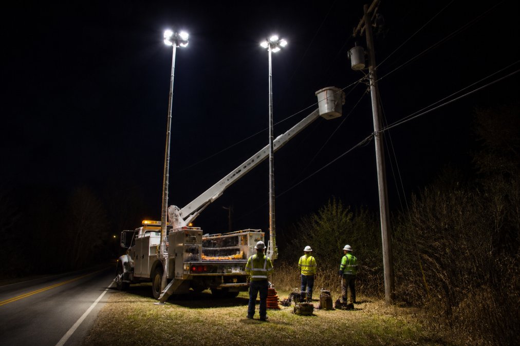 Utility truck with extended LED scene lights illuminating a nighttime roadside work site and crew