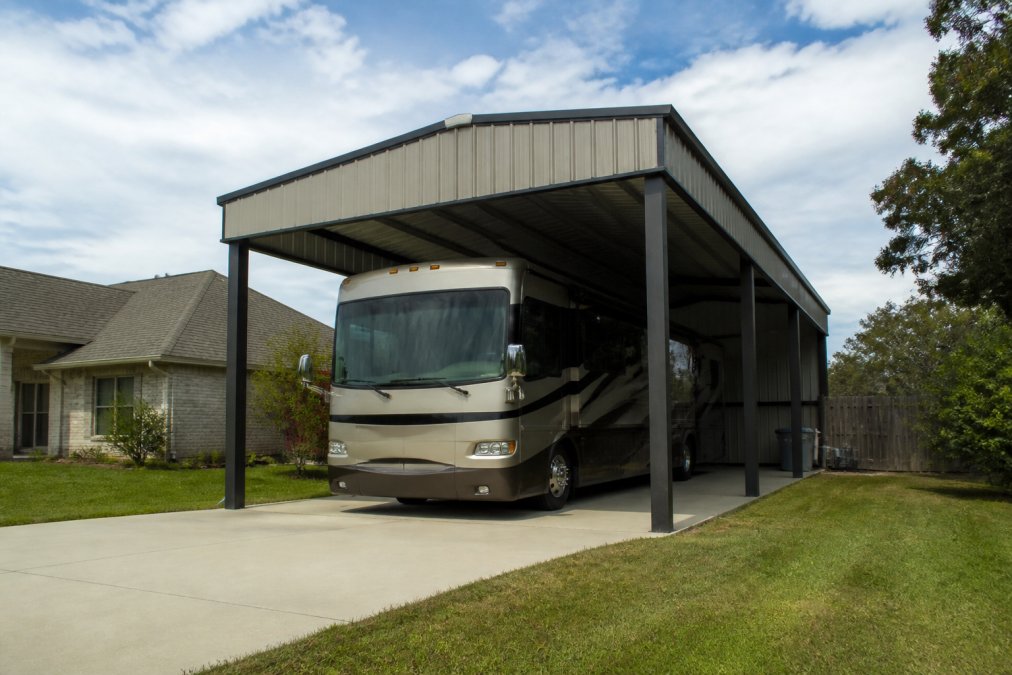 Wide-angle view of a completed metal carport with boxed eave design sheltering an RV, showing the finished aesthetic and weather protection in a residential setting