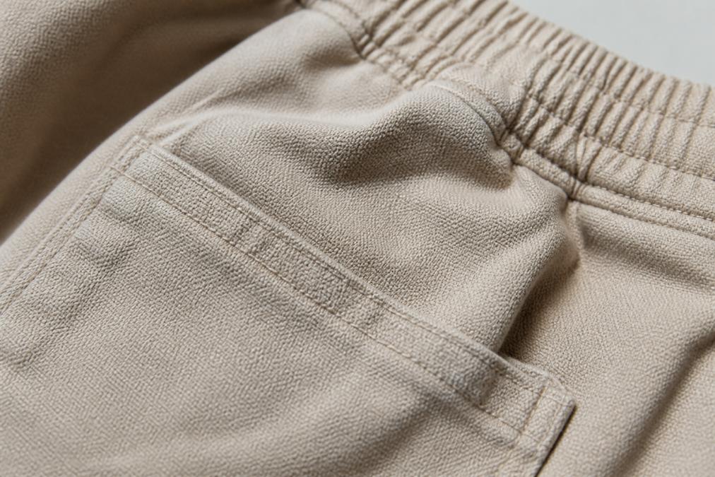 Close-up detail shot of heavyweight cotton fabric showing the texture, weave pattern, and reinforced stitching on the pocket corner and waistband area