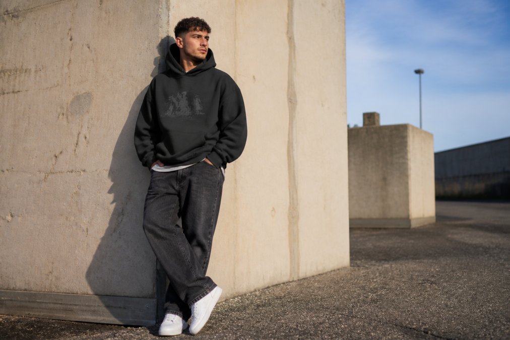 Person wearing an oversized heavyweight hoodie with a bold graphic quote, styled with relaxed jeans and sneakers, standing confidently in natural lighting