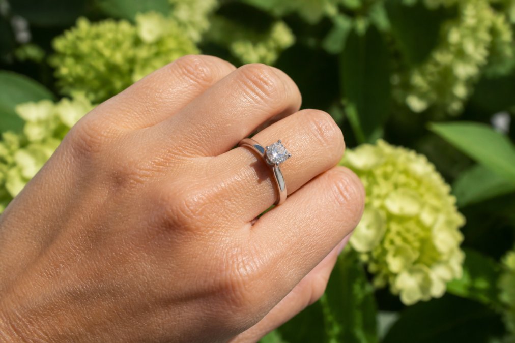 Close-up of a platinum engagement ring being worn on a hand, showing the lustrous white metal surface and secure gemstone setting in natural daylight
