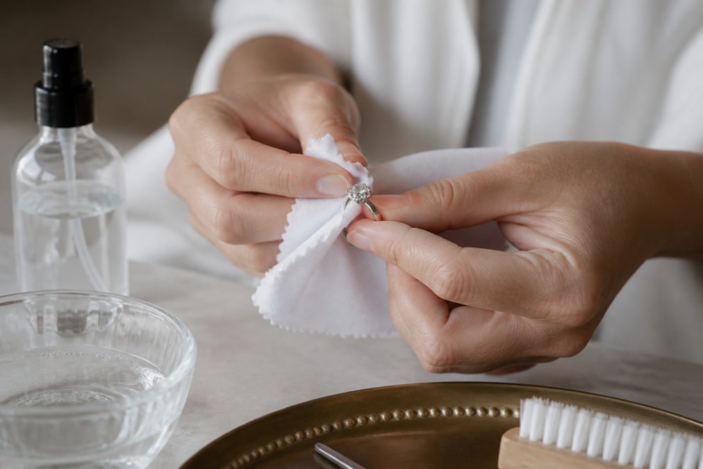 Hands gently cleaning a platinum ring with a soft cloth and jewelry cleaner, demonstrating proper maintenance technique in a home setting