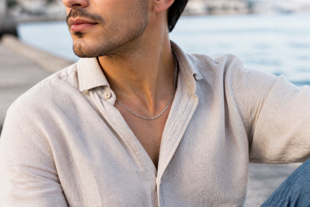Mann trägt silberne Herrenkette zu Casual-Outfit mit Leinenhemd und Jeans, natürliches Tageslicht, Nahaufnahme des Kettendesigns am Hals