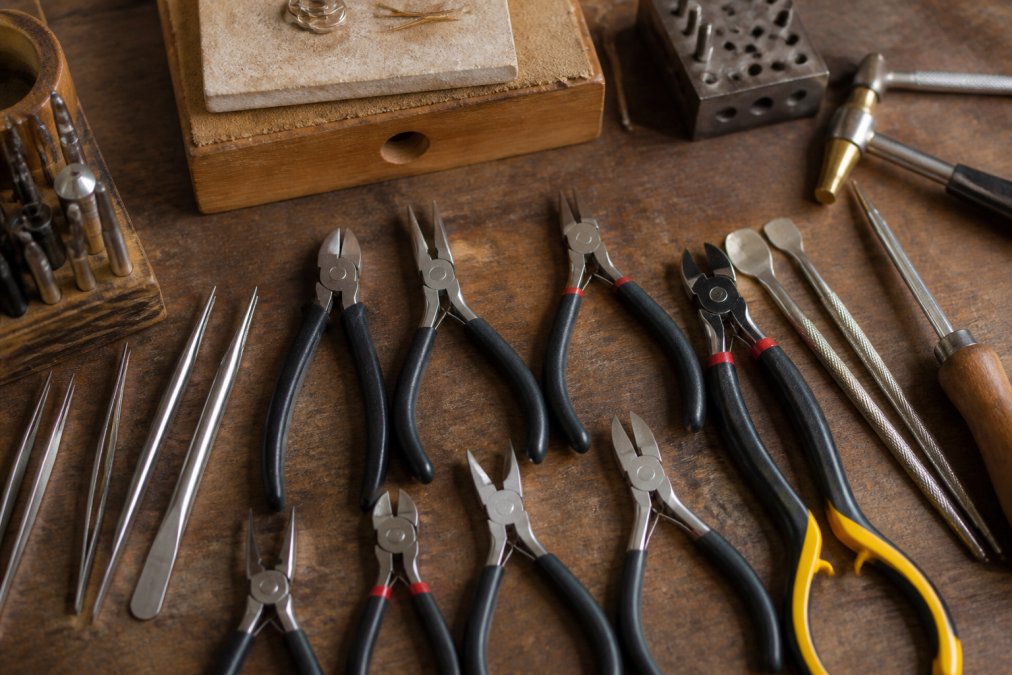 Flat lay of professional jewelry-making tools including pliers, wire cutters, crimpers, and specialty tools arranged neatly on a crafting workbench