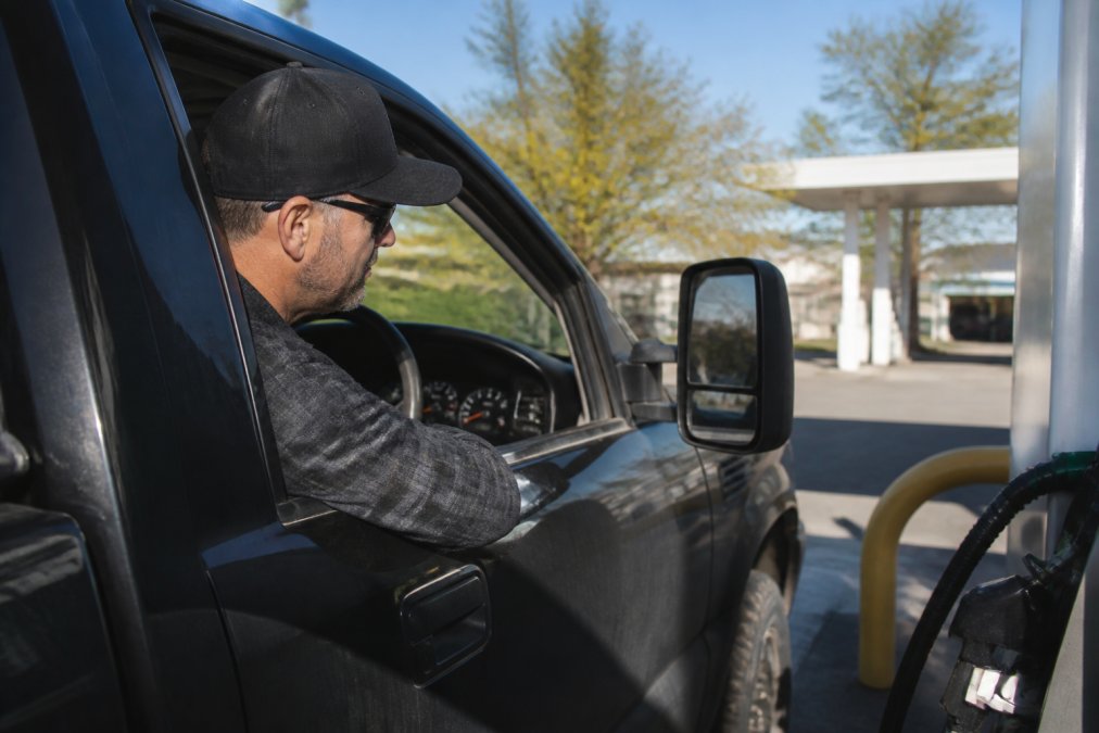 Close-up of a truck driver checking fuel gauge at a gas station, monitoring fuel consumption on a bright afternoon