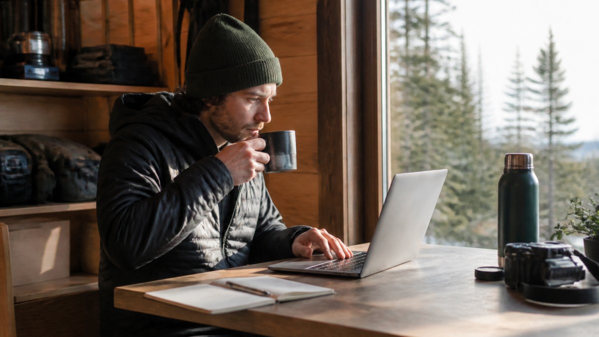 Remote professional at desk with fresh cup of coffee, focused on laptop work during morning hours with bright natural light streaming through window