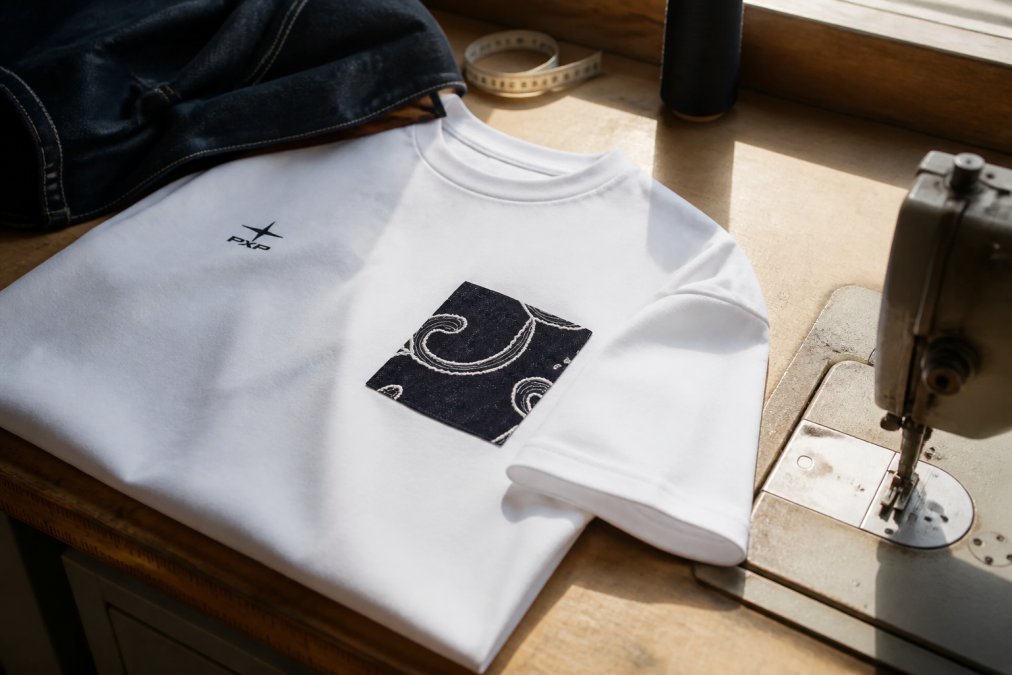 Close-up van premium katoenen stof met zichtbare fijne stiksels, contrasterende naden en handgemaakte afwerkingen op een denim jasje, natuurlijke daglicht op werkbank